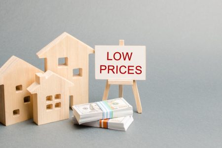 Wooden houses and a poster with the words Low Prices. The concept of reducing the value of real estate. Lower mortgage interest rates. Falling prices for rental housing and apartments. Home sales